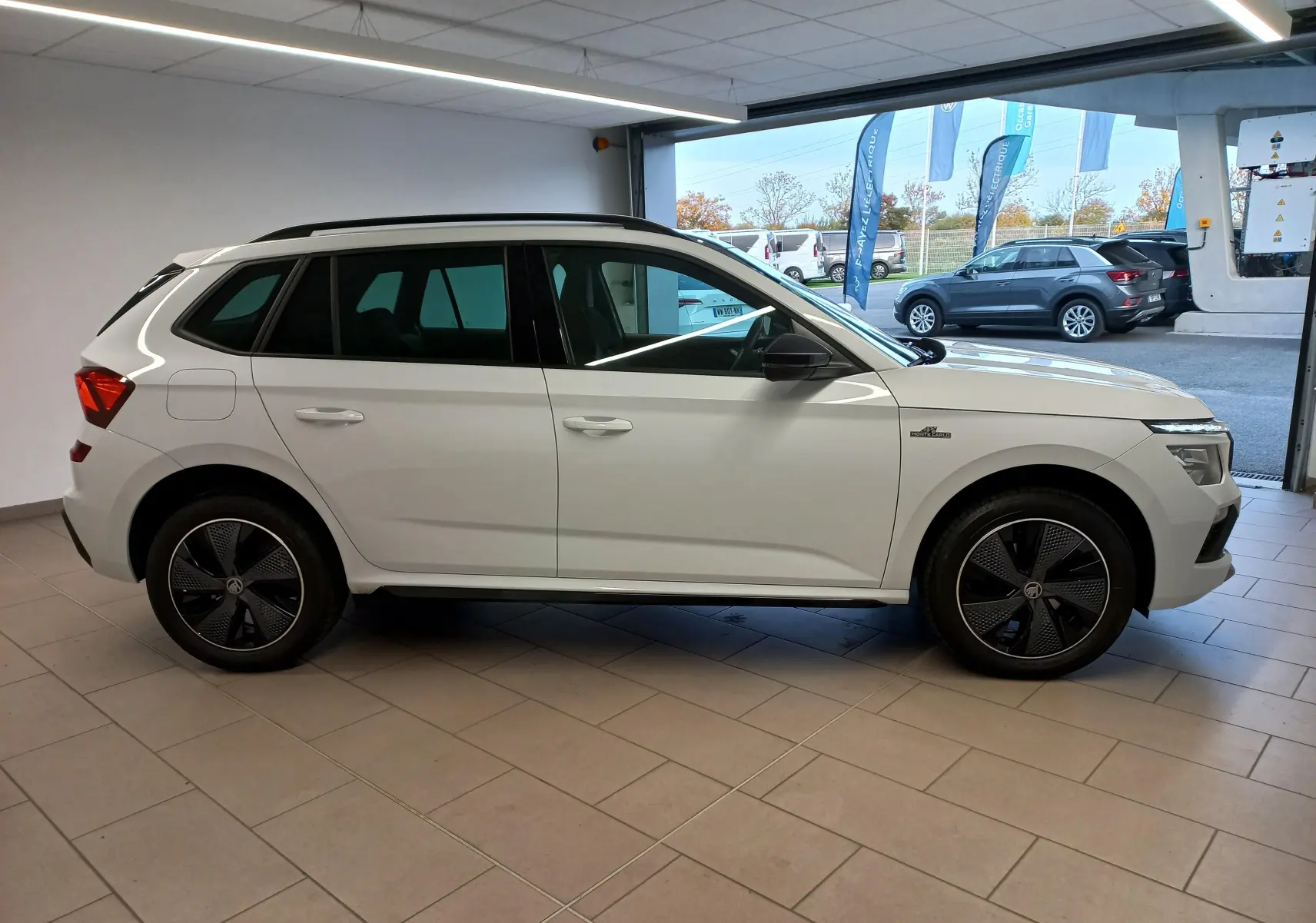 Vue de profil côté gauche d'un Skoda Kamiq 2025 blanc Lune avec jantes noires et badge Monte-Carlo visible sur l'aile avant.