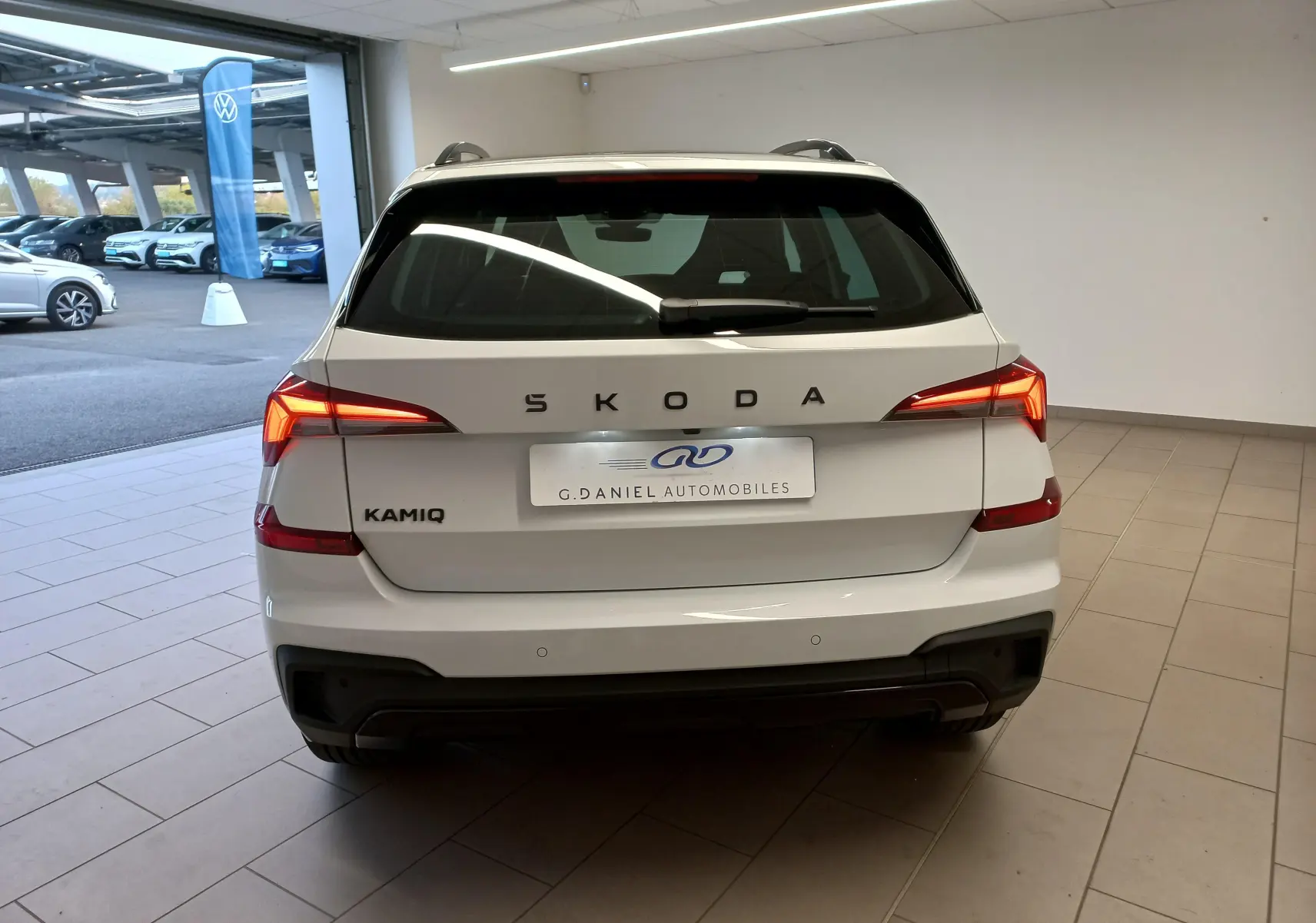 Vue arrière d'un Skoda Kamiq blanc Lune 2025 avec feux allumés et logo SKODA en lettres espacées.