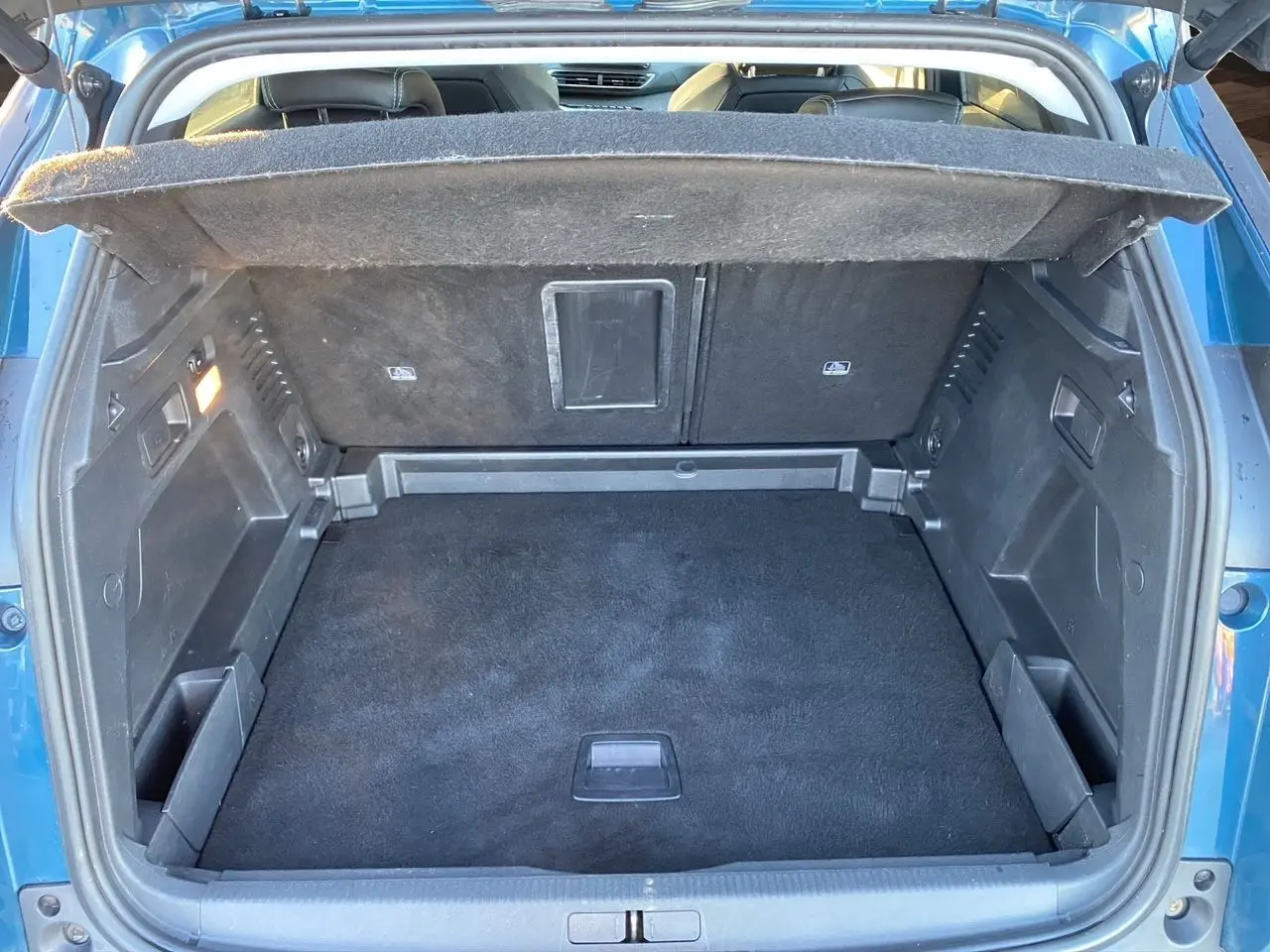 Coffre ouvert vu de l'arrière d'un Peugeot 3008 bleu Célèbes, montrant un espace de chargement propre et spacieux.