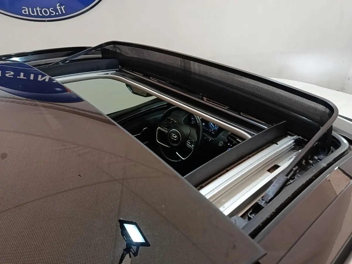 Vue plongeante sur le toit ouvrant électrique ouvert d’un Hyundai Tucson blanc, avec aperçu du tableau de bord intérieur.