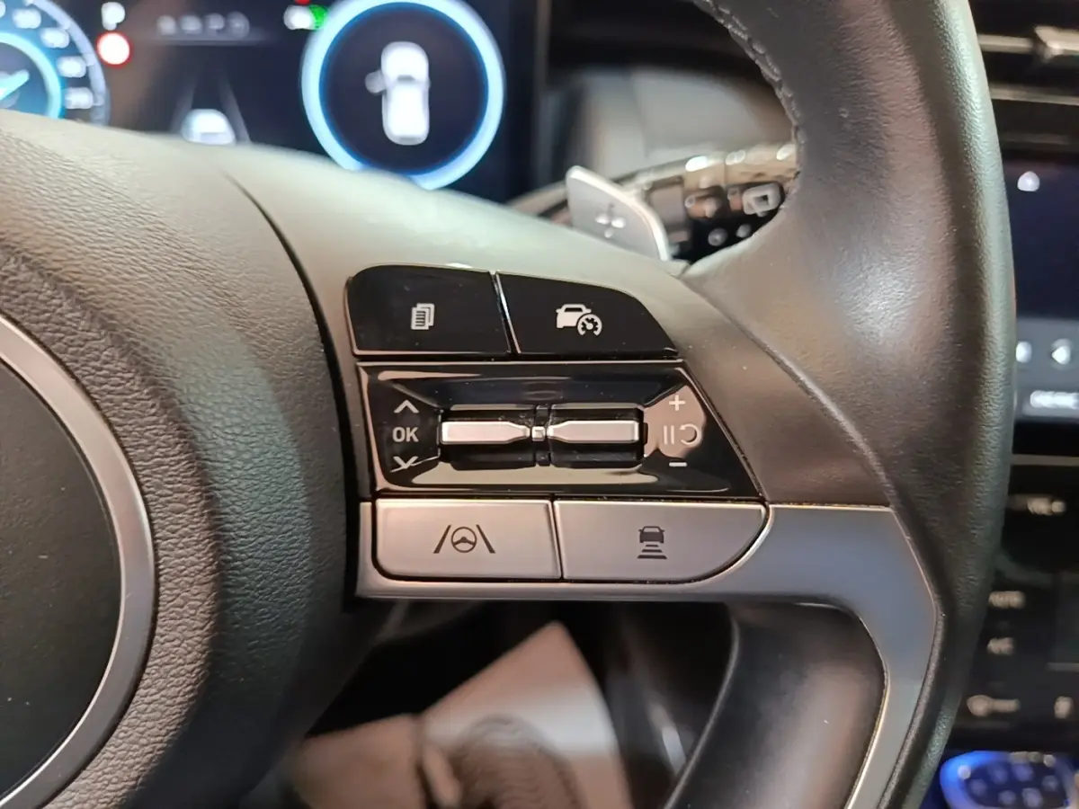 Gros plan sur les commandes du volant noir du Hyundai Tucson 1.6 Hybrid 230 Executive, avec boutons multifonctions visibles.