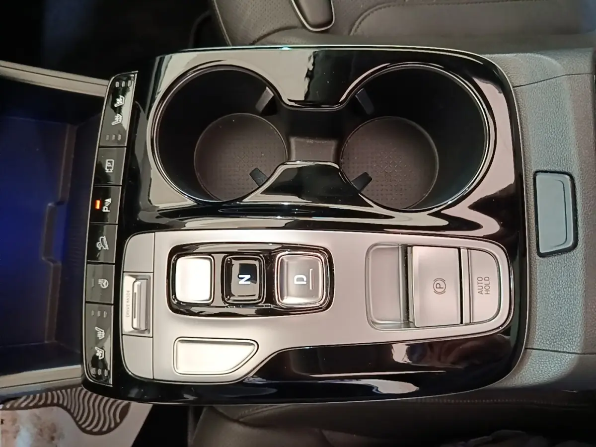 Vue plongeante sur la console centrale noire brillante du Hyundai Tucson 1.6 Hybrid 230 Executive avec commandes de boîte auto et porte-gobelets.