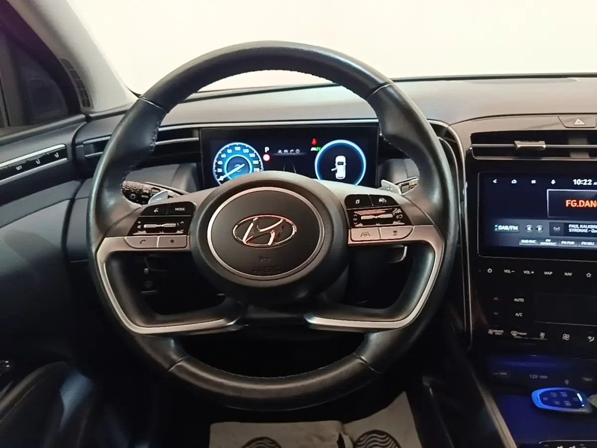 Vue intérieure centrée sur le volant noir du Hyundai Tucson 1.6 Hybrid 230 Executive avec tableau de bord digital.