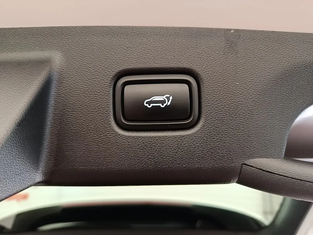 Bouton noir d'ouverture électrique du coffre sur la garniture intérieure d'un Hyundai Tucson blanc, vue rapprochée.