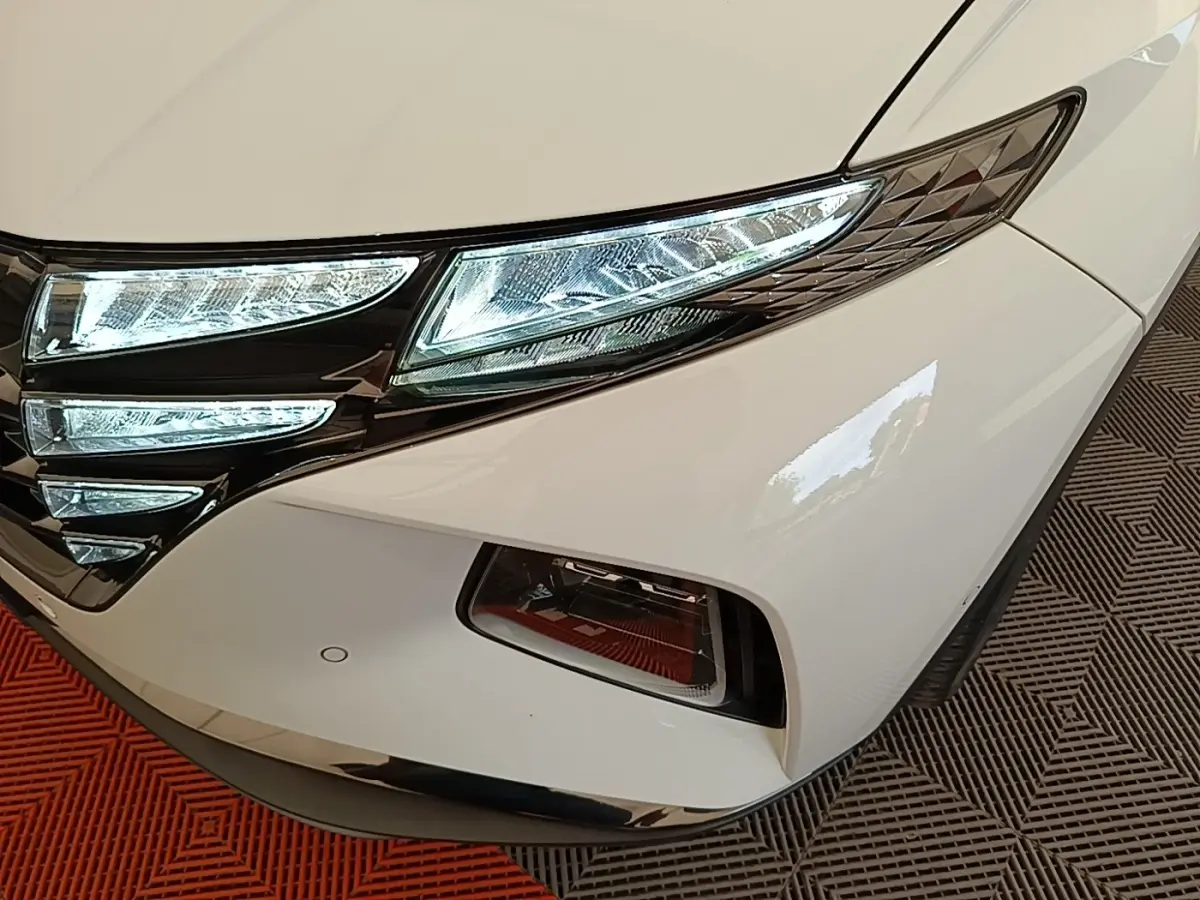 Gros plan sur l’avant droit blanc du Hyundai Tucson 1.6 Hybrid 230 Executive avec phares LED allumés.