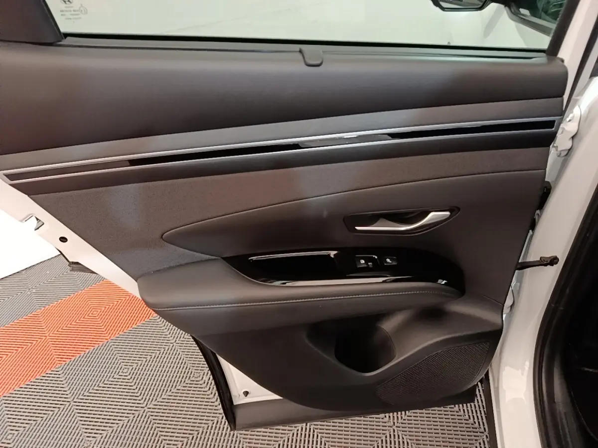 Vue intérieure de la porte avant droite du Hyundai Tucson blanc 2022, avec garniture noire et commandes électriques.