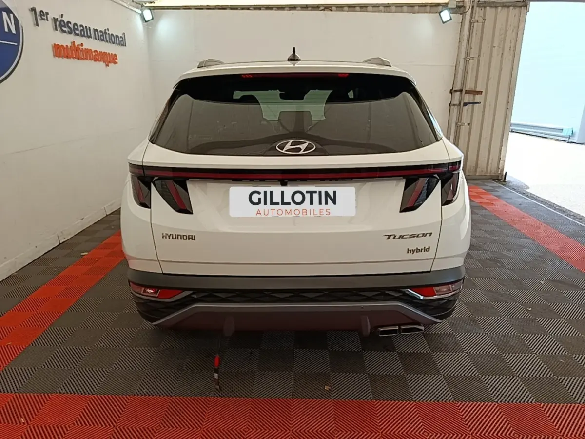 Vue arrière d'un Hyundai Tucson blanc hybride 2022 avec feux arrière LED et logo Hyundai visible.