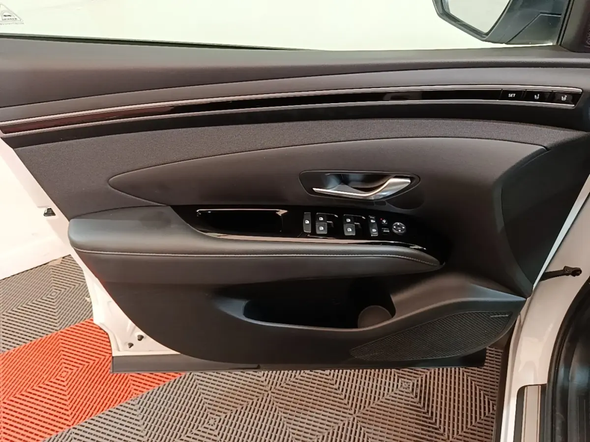 Vue intérieure de la porte avant gauche blanche d'un Hyundai Tucson 1.6 Hybrid 230 Executive avec commandes et habillage noir.