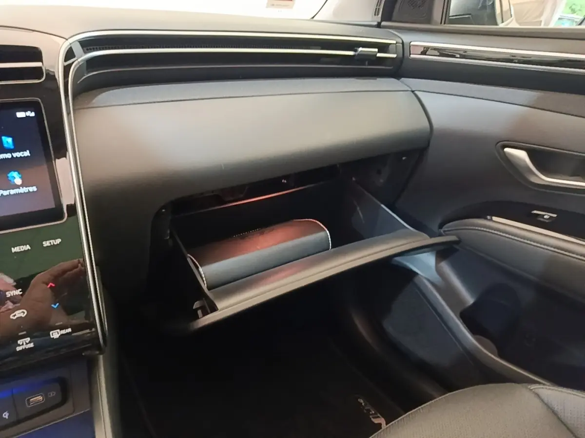 Vue intérieure côté passager du tableau de bord noir avec boîte à gants ouverte du Hyundai Tucson blanc 2022 hybride.