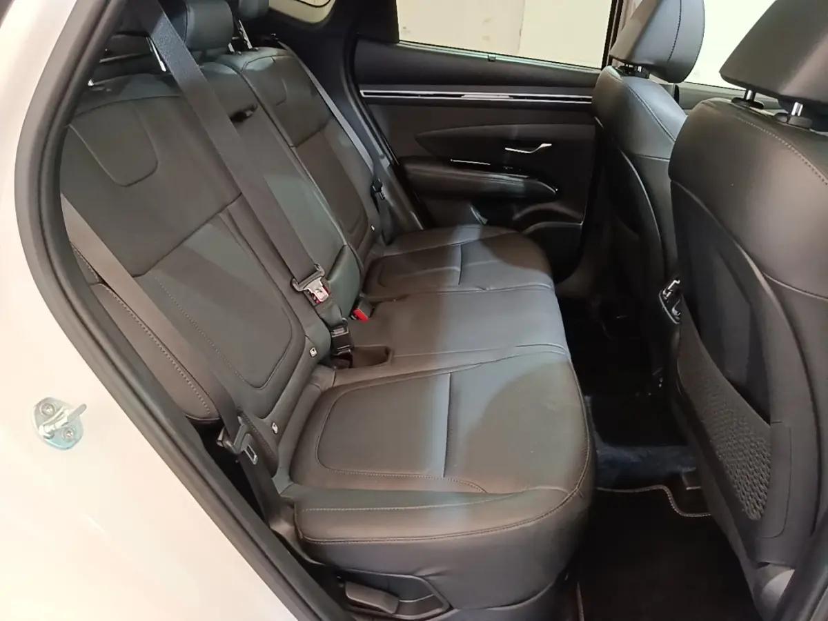 Vue intérieure côté arrière gauche du Hyundai Tucson 1.6 Hybrid 230 Executive 2022, sièges en cuir noir et portière blanche ouverte.