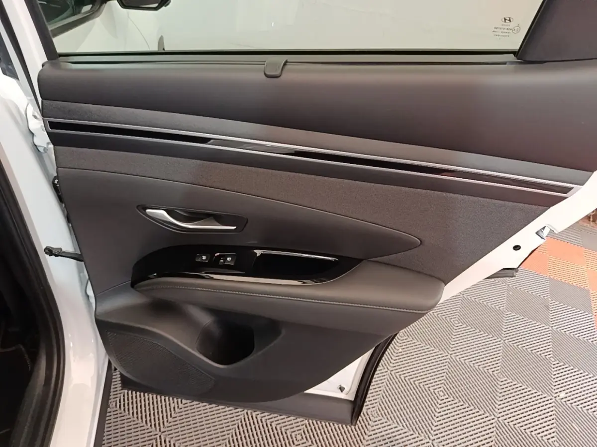 Vue intérieure de la porte arrière gauche blanche du Hyundai Tucson 1.6 Hybrid 230 Executive avec garniture noire et commandes de fenêtre.