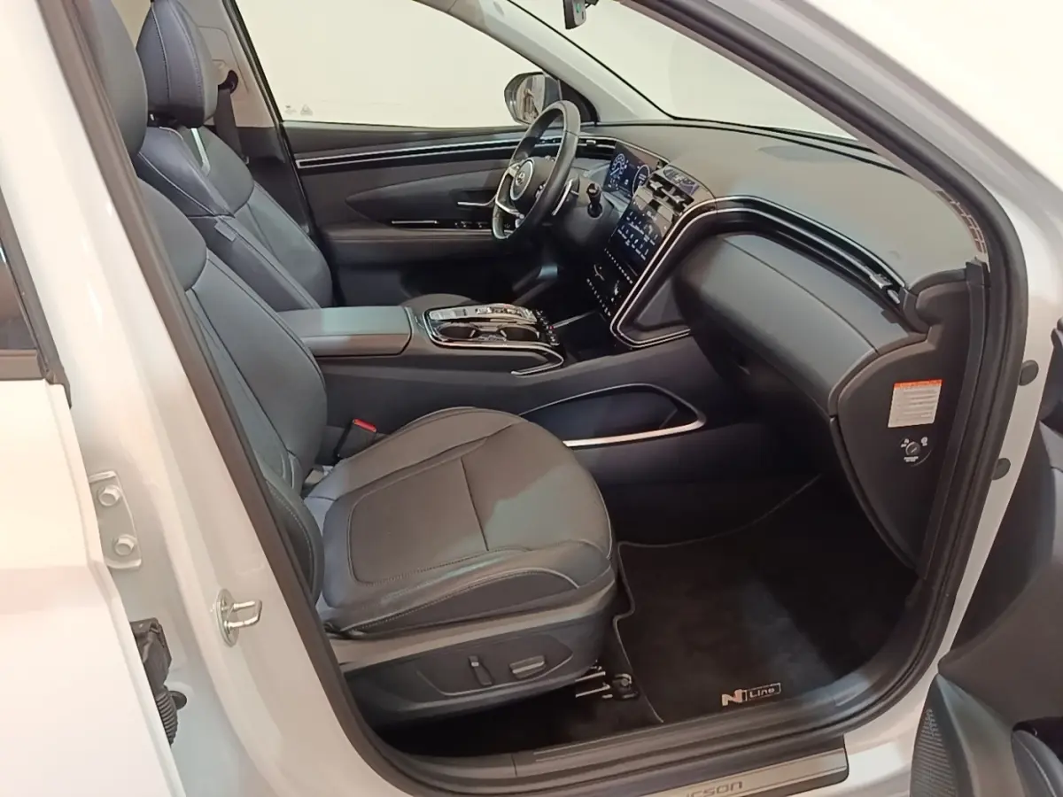 Vue intérieure côté conducteur du Hyundai Tucson blanc 2022, avec sièges cuir noirs et tableau de bord moderne.