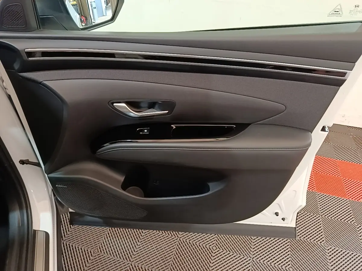 Vue intérieure de la porte avant gauche du Hyundai Tucson blanc, avec garniture noire et poignée argentée.