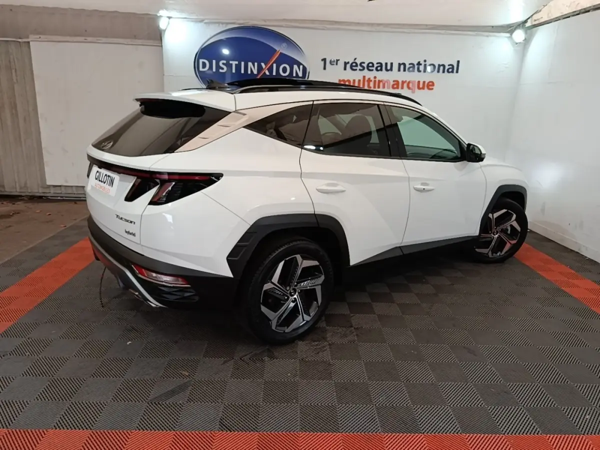 Vue 3/4 arrière droite d’un Hyundai Tucson blanc 2022 avec jantes noires et toit noir dans un showroom.