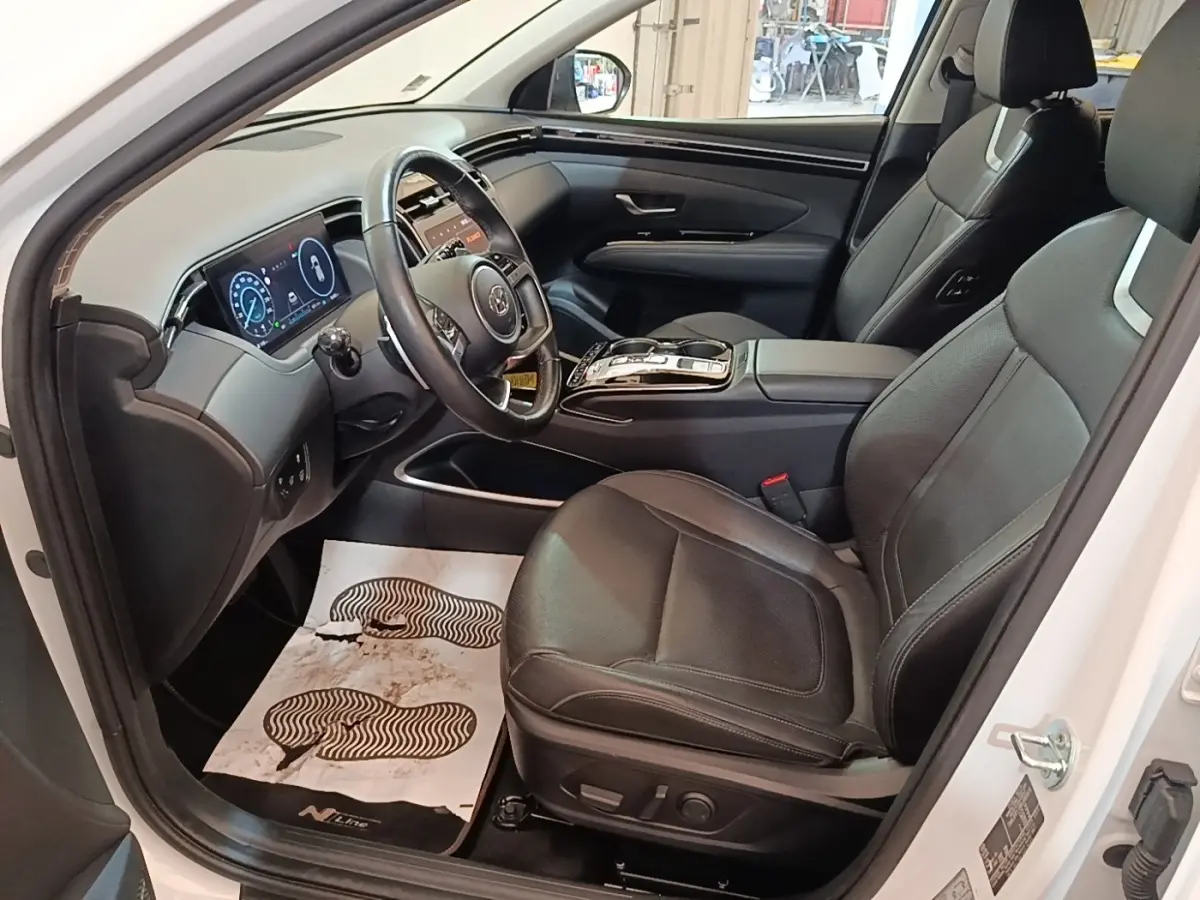 Vue intérieure côté conducteur du Hyundai Tucson blanc 2022, sièges cuir noirs et tableau de bord digital lumineux.