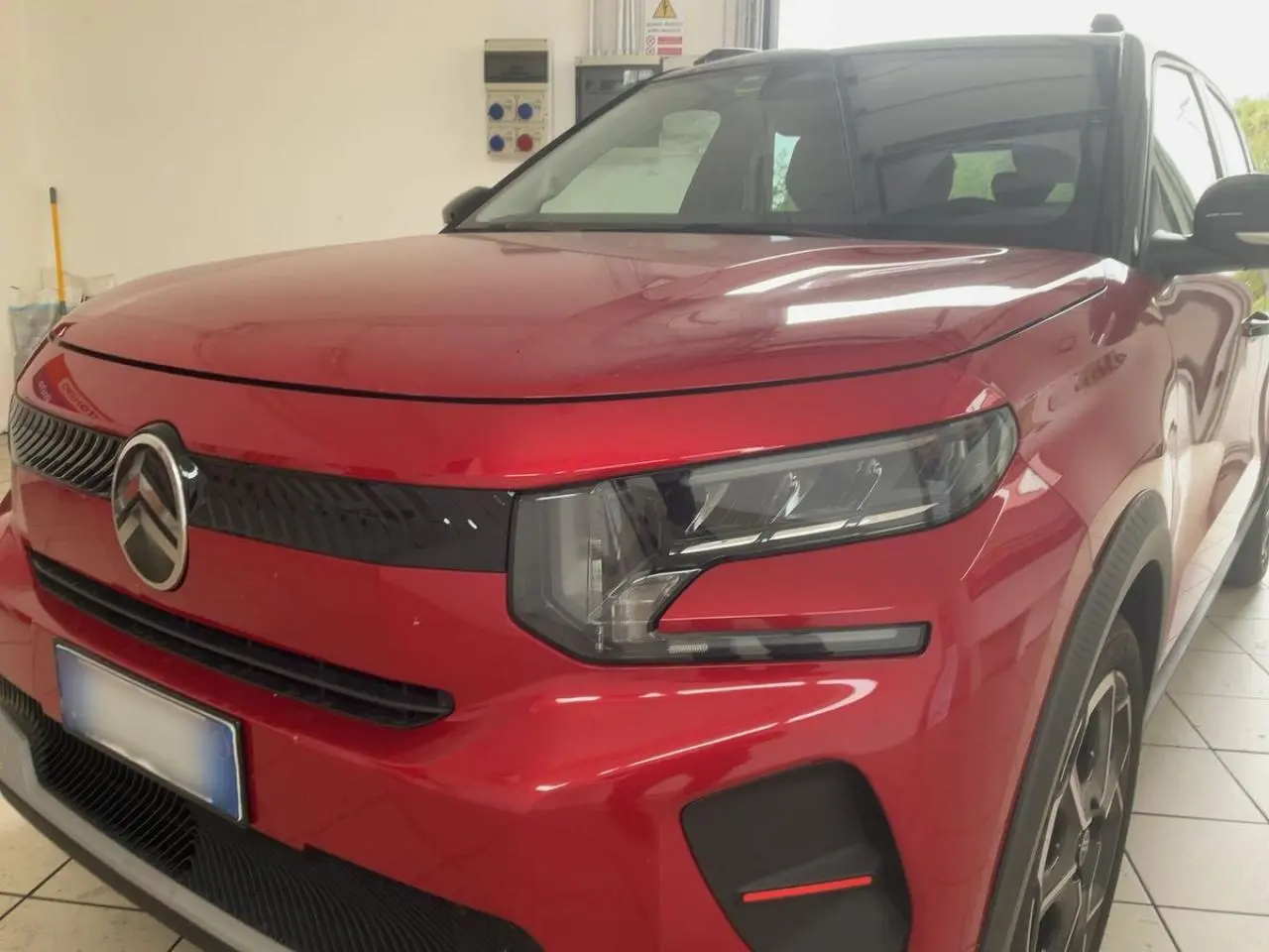 Vue 3/4 avant droite d'une Citroën C3 ë-113 Berline Max rouge métal foncé avec calandre noire et phares modernes.
