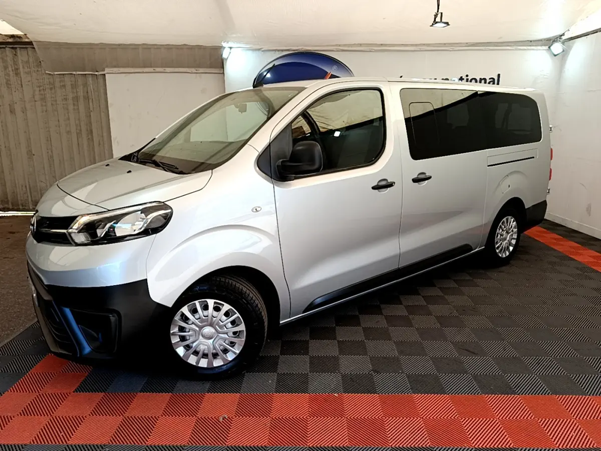Vue côté gauche en 3/4 avant d'un Toyota Proace Verso gris clair avec vitres arrière teintées et jantes acier.
