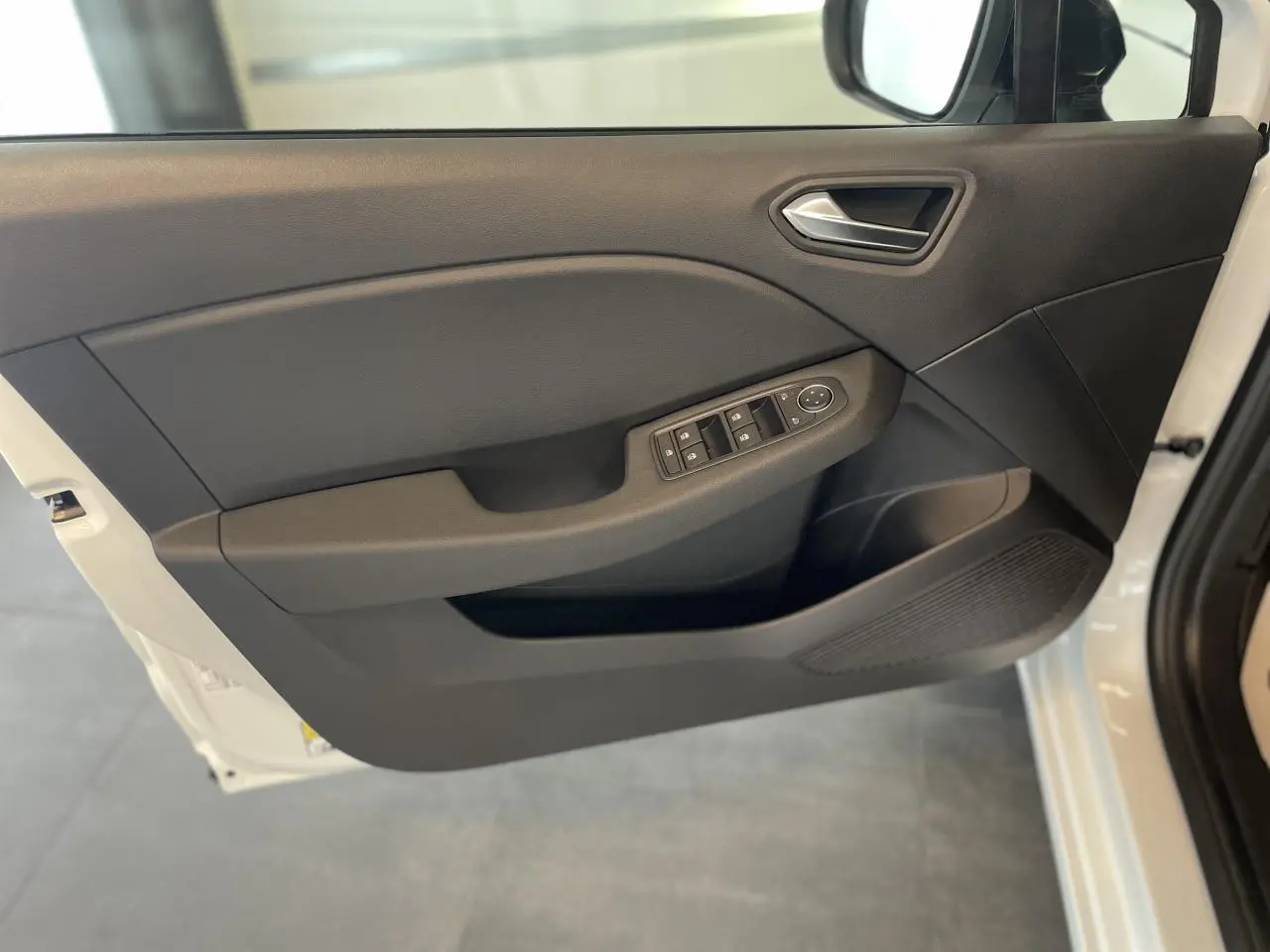 Porte avant gauche ouverte de la Renault Clio blanche, avec commandes électriques des vitres et poignée intégrée.