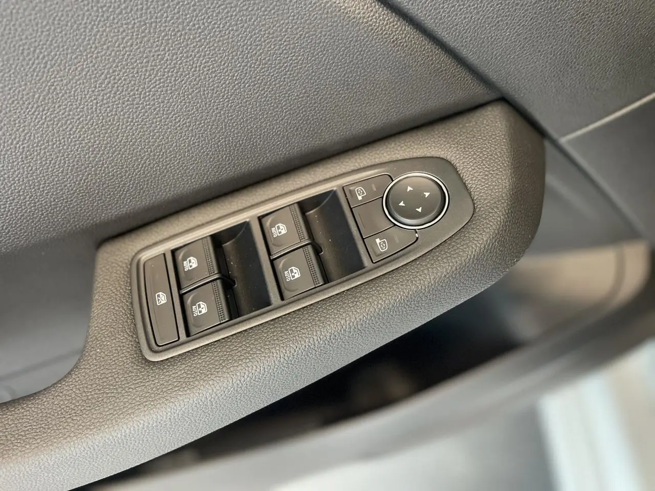 Gros plan sur les commandes de lève-vitres et rétroviseurs côté conducteur de la Renault Clio blanche 2025.