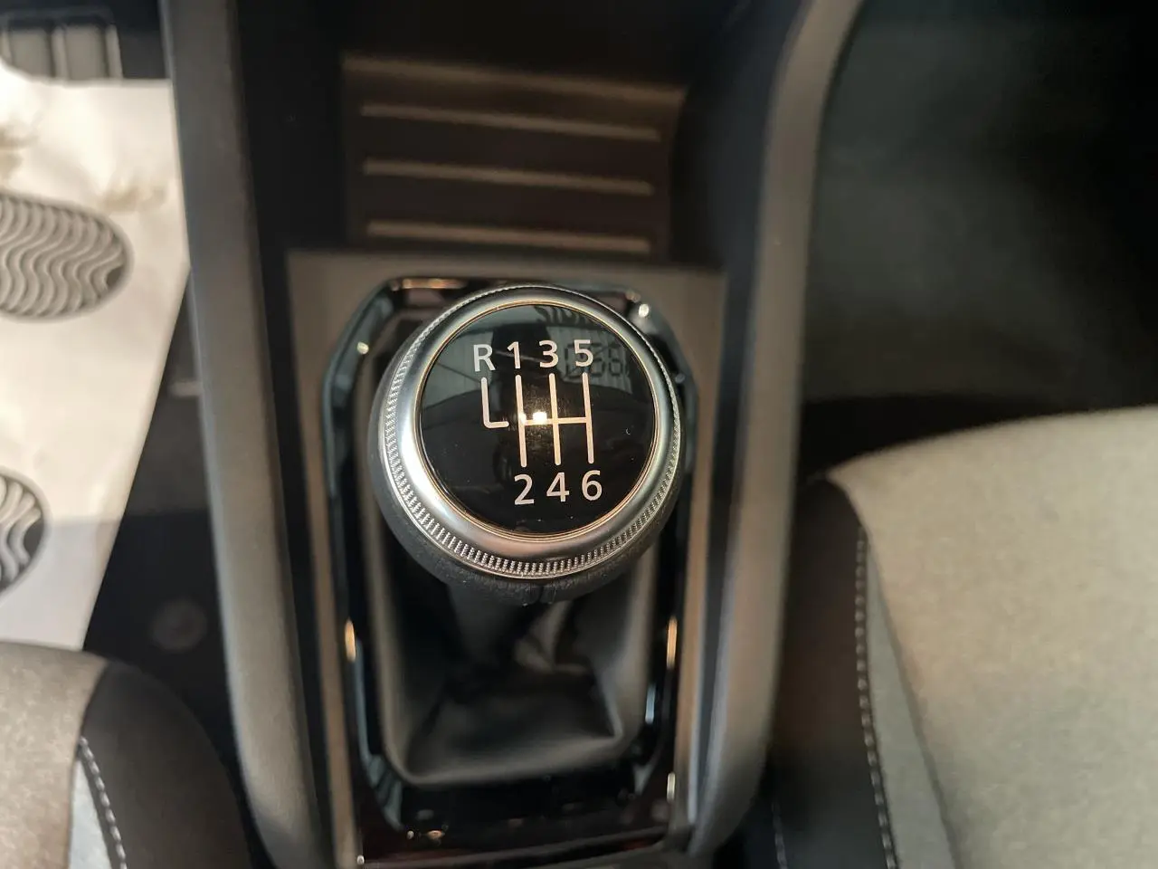 Gros plan sur le levier de vitesses manuel de la Renault Clio blanche, entouré de la console noire et sièges gris.