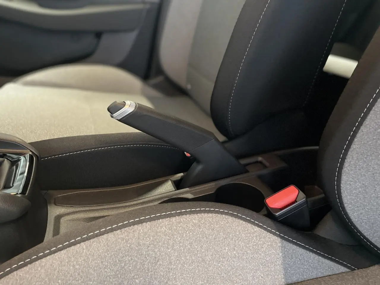 Gros plan sur frein à main manuel et ceinture rouge entre sièges tissu gris et noir de Renault Clio 1.5 Blue dCi 2025.
