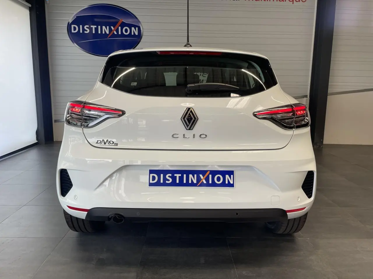 Vue arrière d'une Renault Clio blanche 2025 avec feux LED et logo chromé dans un showroom.