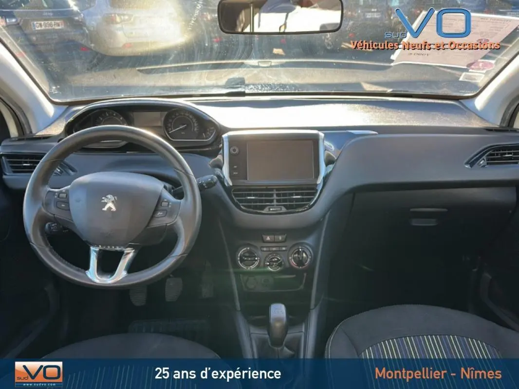 Vue intérieure avant du tableau de bord noir de la Peugeot 208 blanche de 2015 avec écran tactile et volant multifonction.
