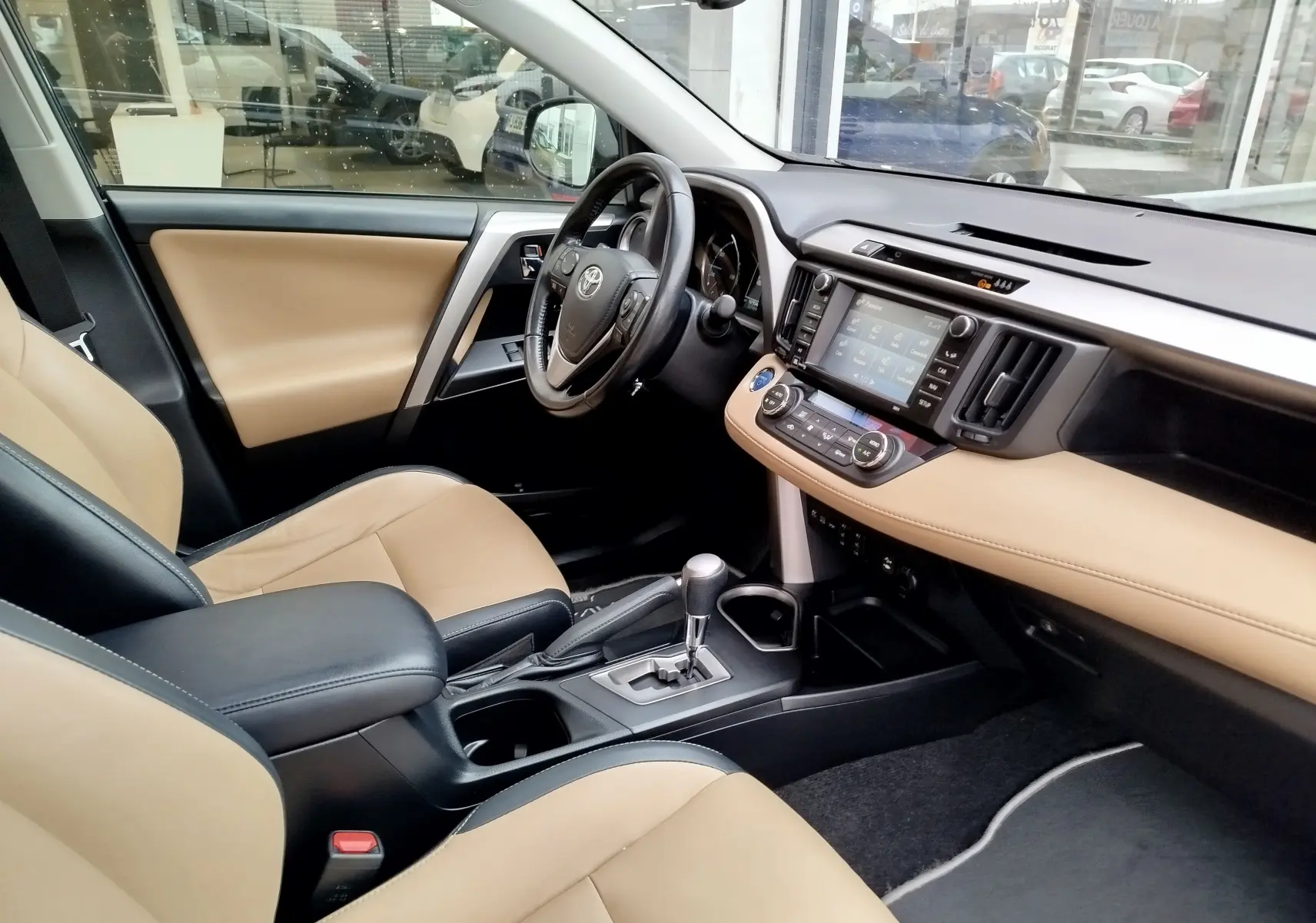 Intérieur beige et noir du Toyota RAV4 2017, vue côté conducteur montrant tableau de bord et console centrale moderne.