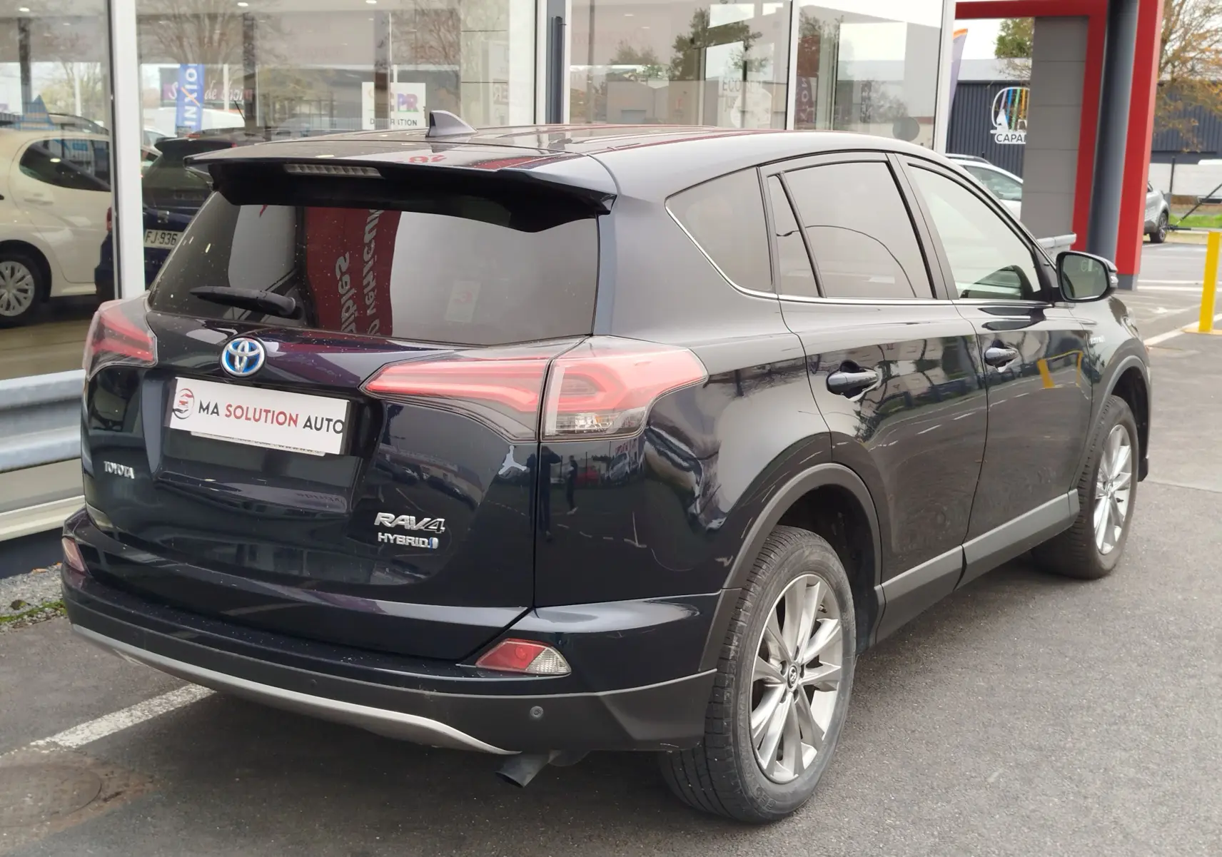 Toyota RAV4 hybride noir cobalt vu en 3/4 arrière droit, avec feux arrière LED et jantes alliage visibles.
