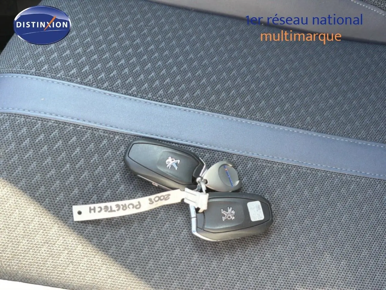 Gros plan sur les clés noires de la Peugeot 2008 posées sur un siège en tissu gris à motif.