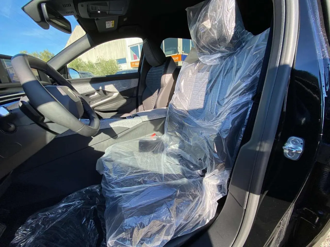 Intérieur du Peugeot 3008 noir 2025 vu côté conducteur, siège avant protégé par une housse plastique.