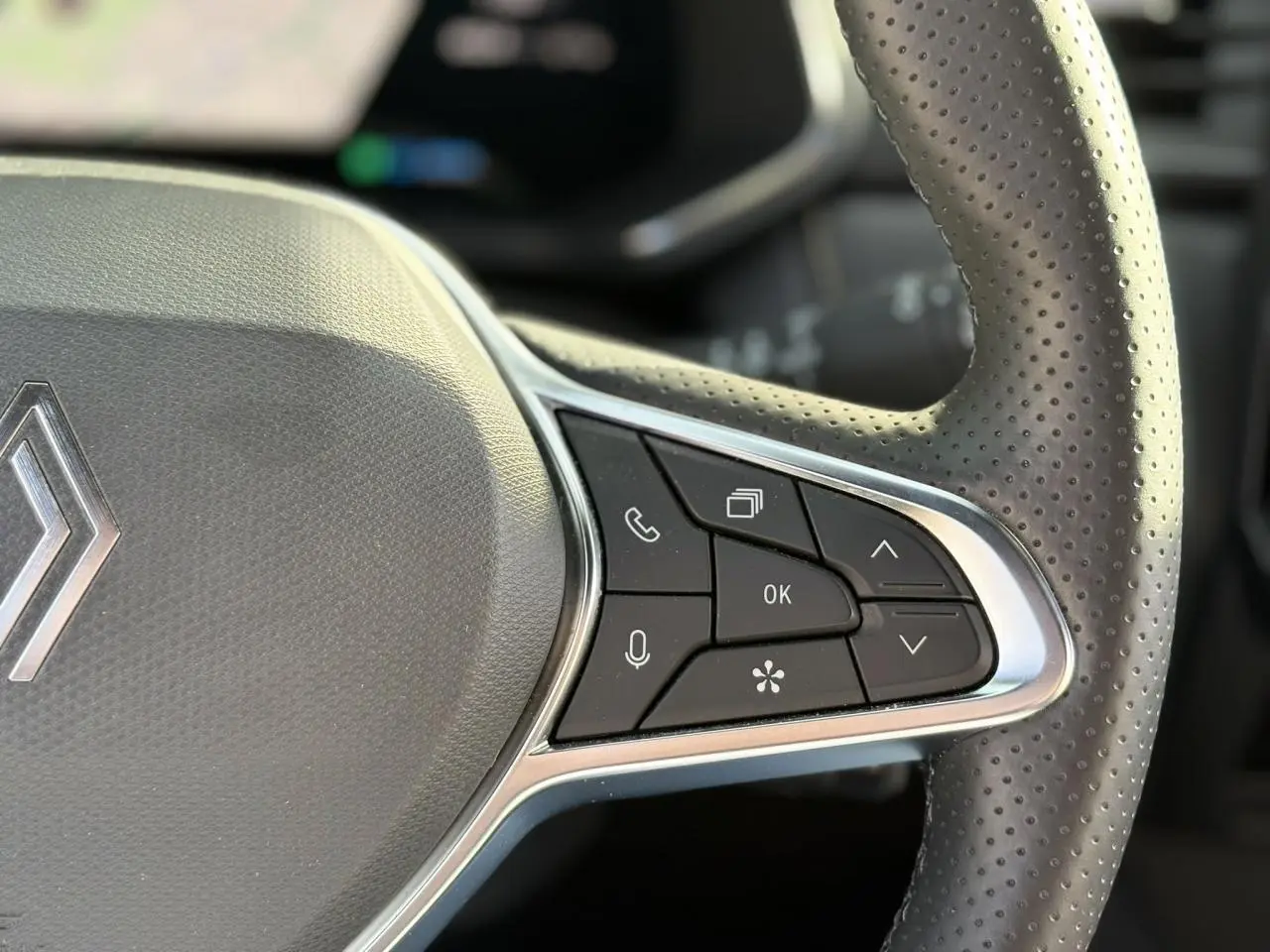 Gros plan sur le côté droit du volant en cuir perforé noir du Renault Symbioz avec commandes intégrées et logo Renault visible.