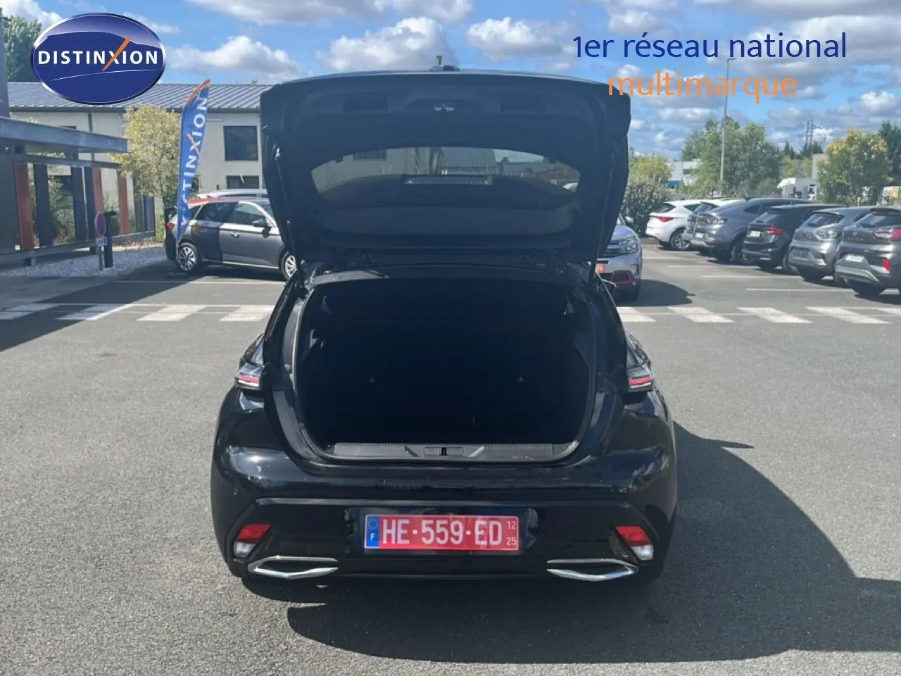 Vue arrière d'une Peugeot 308 noir métal 2025 avec coffre ouvert sur un parking ensoleillé.