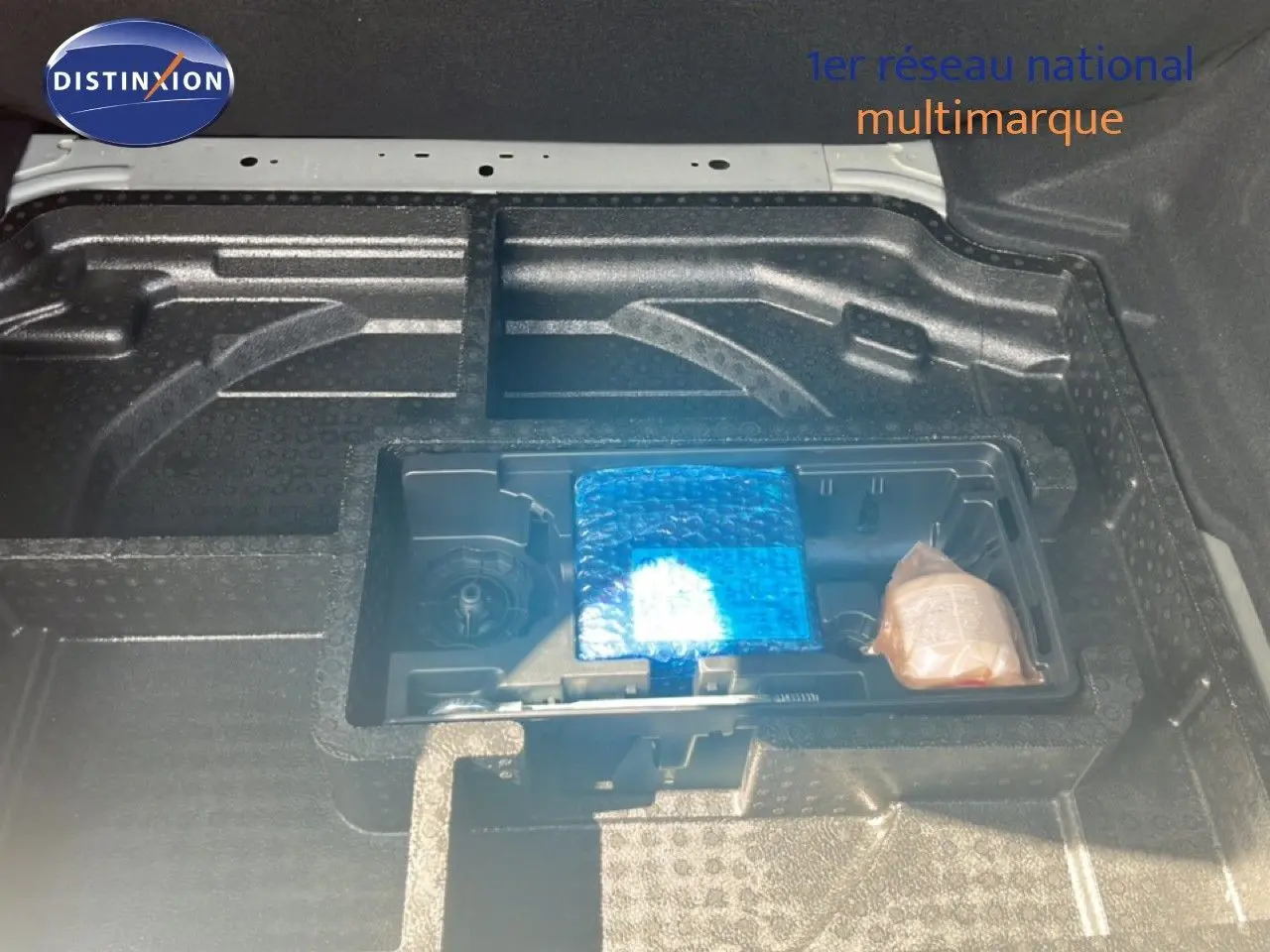 Coffre ouvert de Peugeot 308 noir métal, vue plongeante sur rangement sous plancher avec accessoires emballés.