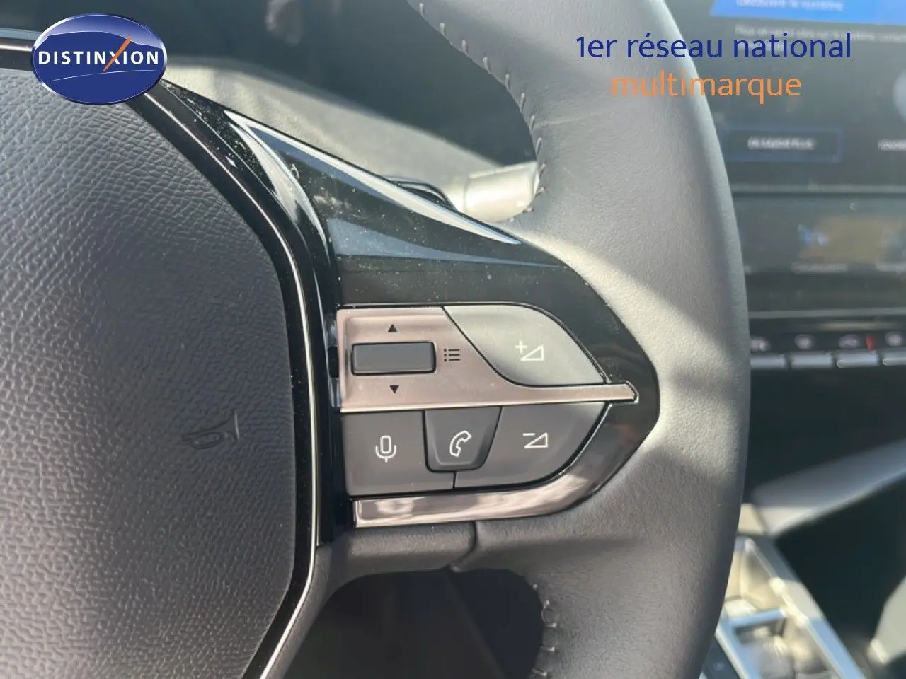 Gros plan sur les commandes gauche du volant cuir noir de la Peugeot 308 Hybrid 2025, avec tableau de bord en arrière-plan.