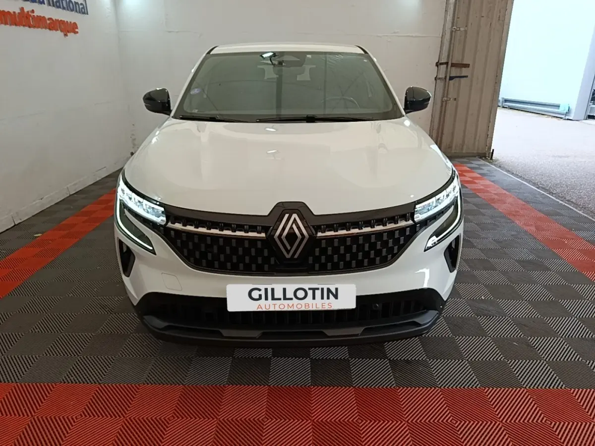 Vue de face du Renault Austral blanc avec calandre noire et phares LED allumés en intérieur showroom.