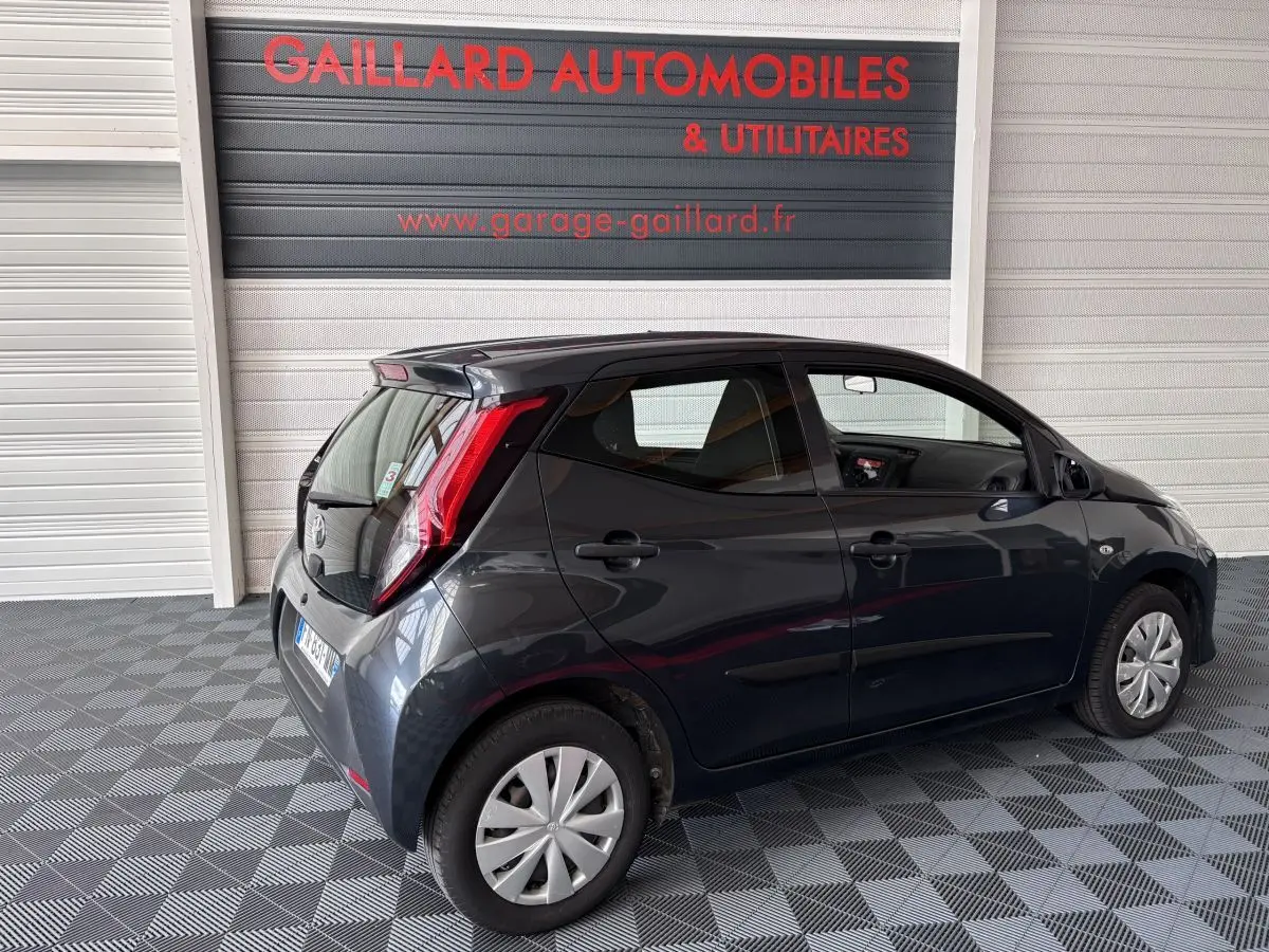 Toyota Aygo 1.0 VVT-i x-black gris foncé vue 3/4 arrière droit dans un garage avec sol damier.