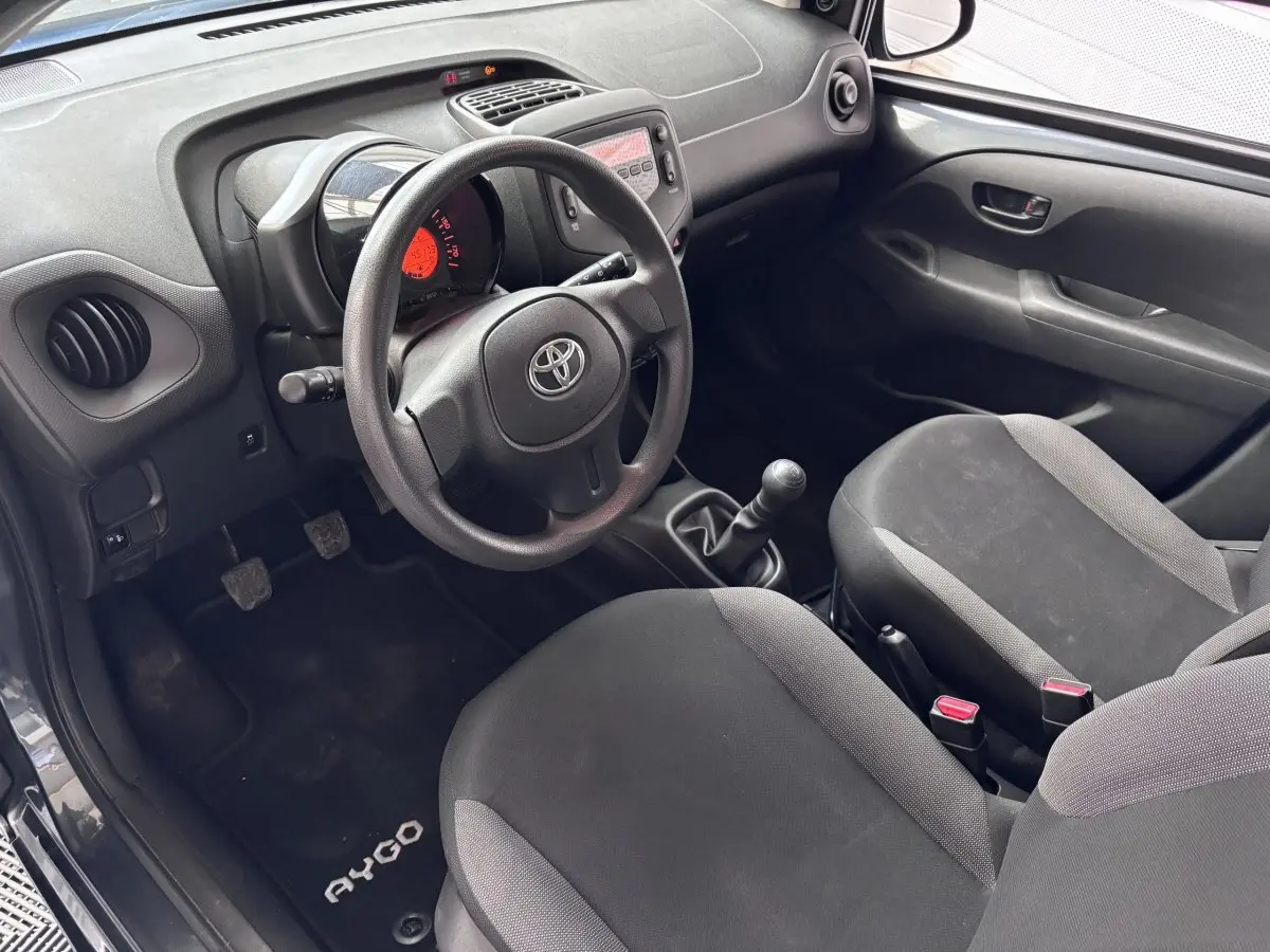 Intérieur avant droit de la Toyota Aygo 1.0 VVT-i x-black 2020, volant, tableau de bord et sièges noirs visibles.