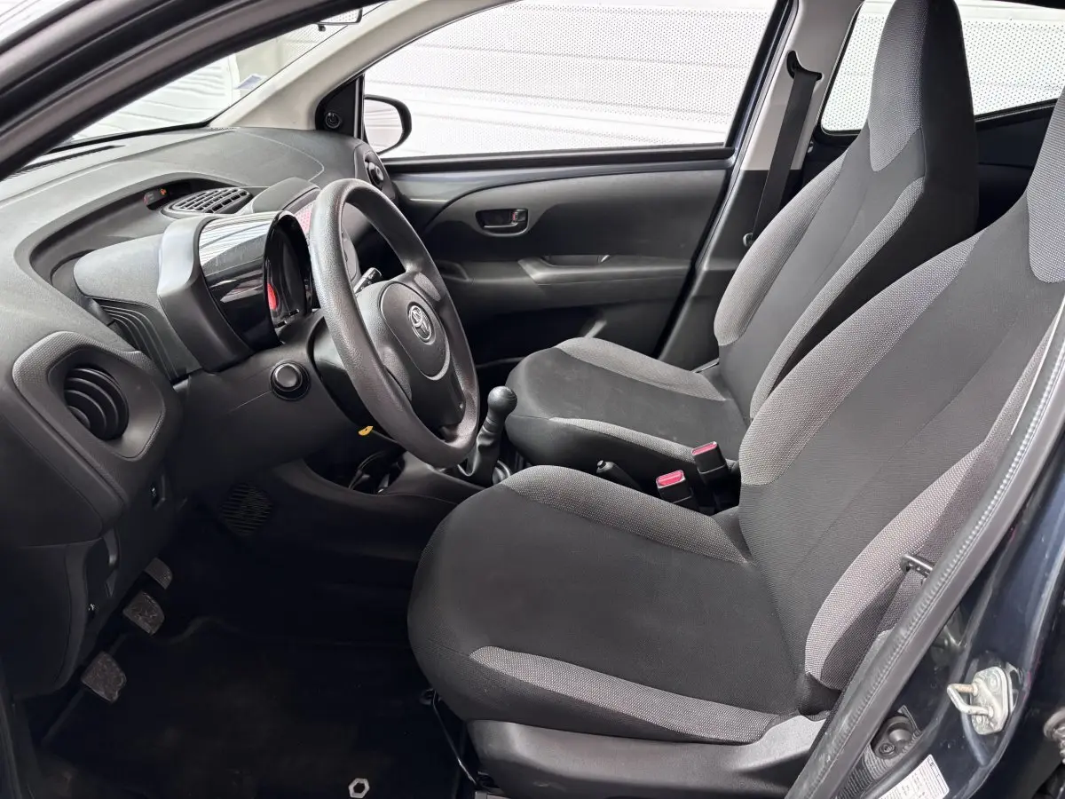 Vue intérieure côté conducteur de la Toyota Aygo 2020, sièges gris et tableau de bord avec volant et levier de vitesse.