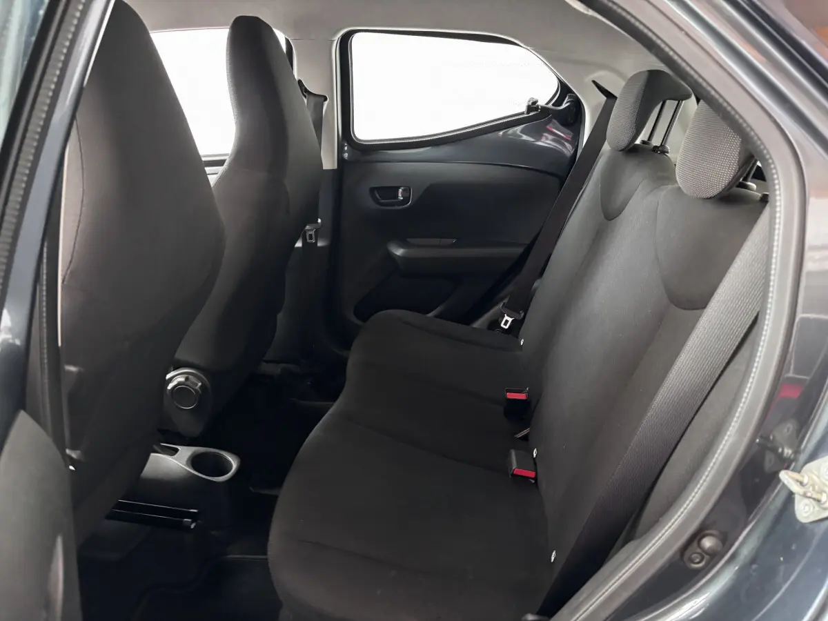 Vue intérieure sur la banquette arrière noire d'une Toyota Aygo gris foncé, avec ceintures et appuie-têtes visibles.