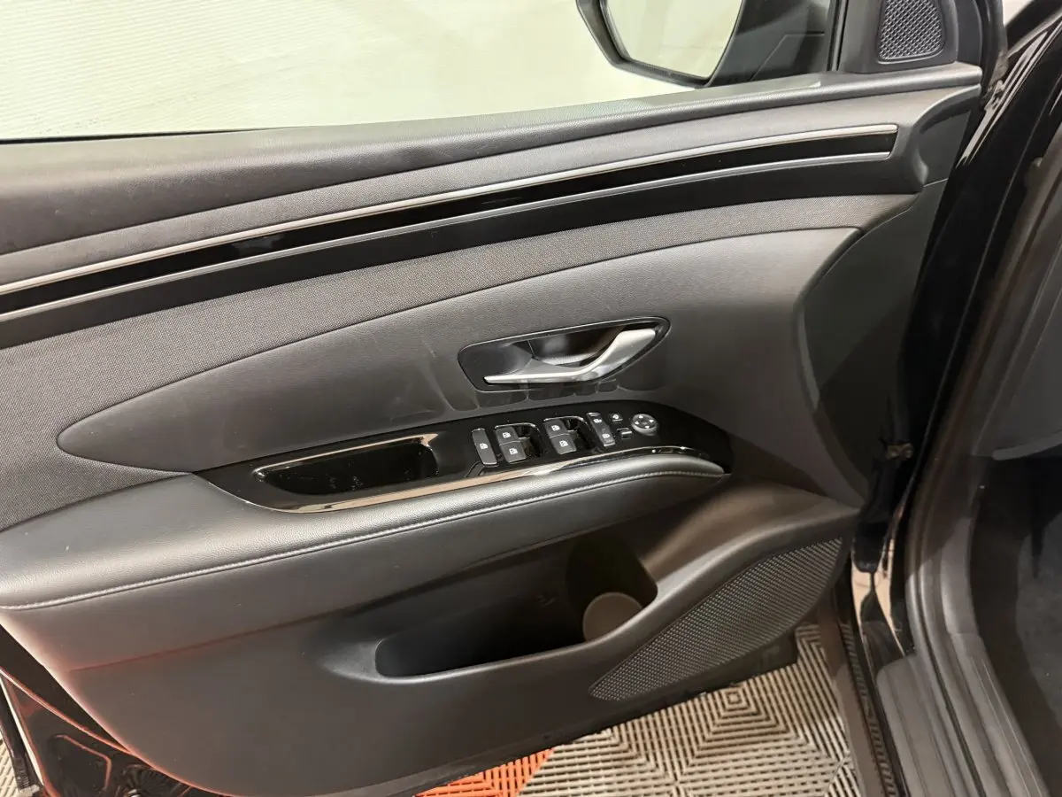 Vue intérieure du panneau de porte côté conducteur du Hyundai Tucson noir, avec commandes électriques et poignée argentée.