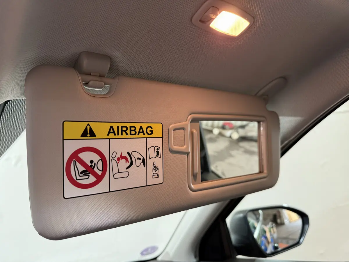 Pare-soleil côté conducteur beige avec miroir intégré et avertissement airbag, rétroviseur extérieur noir visible sur Hyundai Tucson 2021.