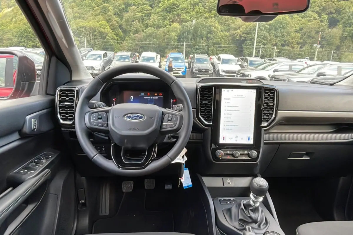 Vue intérieure centrée sur le tableau de bord et volant du Ford Ranger rouge racing 2025 avec boîte manuelle.