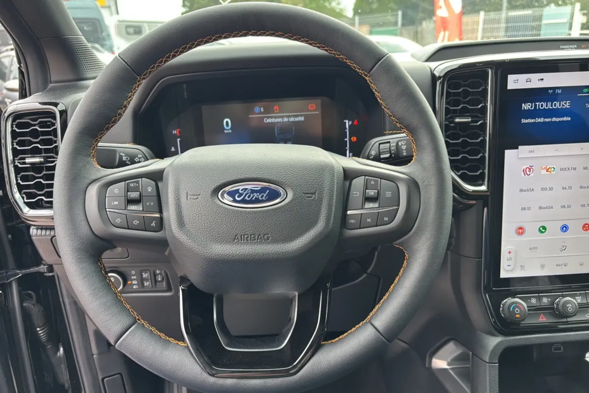 Vue rapprochée du volant noir avec surpiqûres marron du Ford Ranger 2025, tableau de bord et écran tactile visibles.