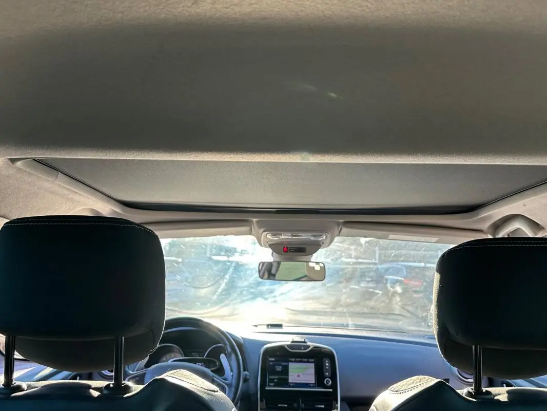 Vue intérieure avant de la Renault Clio IV blanche, montrant tableau de bord avec écran tactile et volant cuir.