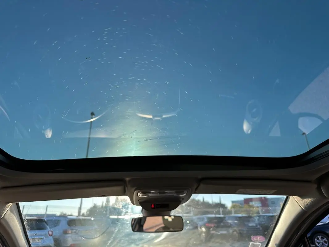 Vue intérieure avant de la Renault Clio IV blanche avec toit panoramique et rétroviseur central visible.