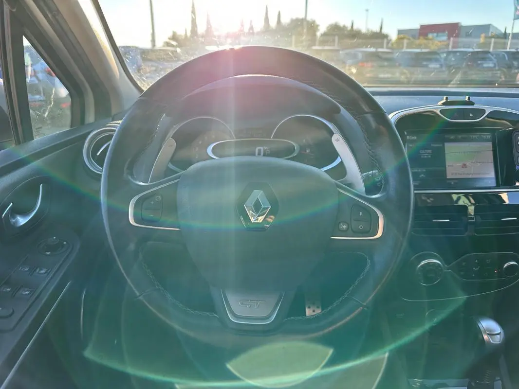 Vue intérieure centrée sur le volant cuir GT d'une Renault Clio IV blanche avec tableau de bord et écran tactile.