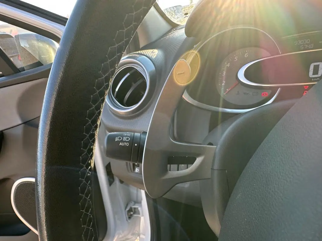 Gros plan sur le volant cuir et le tableau de bord de la Renault Clio IV blanche, avec compteur digital et lumière naturelle.