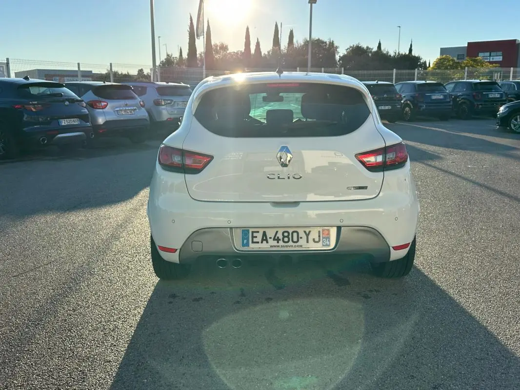 Vue arrière d'une Renault Clio IV TCe 120 GT blanche garée en extérieur avec feux arrière allumés et double sortie d'échappement.