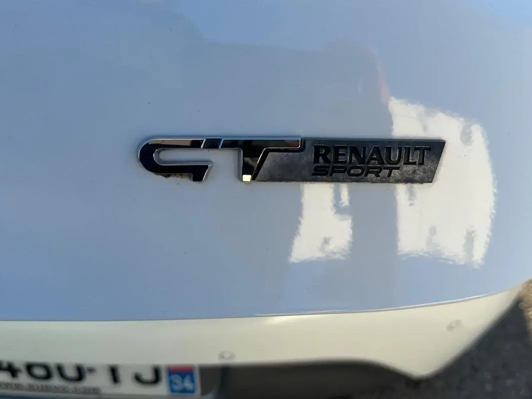 Gros plan sur l'emblème GT Renault Sport en chrome sur la carrosserie blanche arrière de la Renault Clio IV.